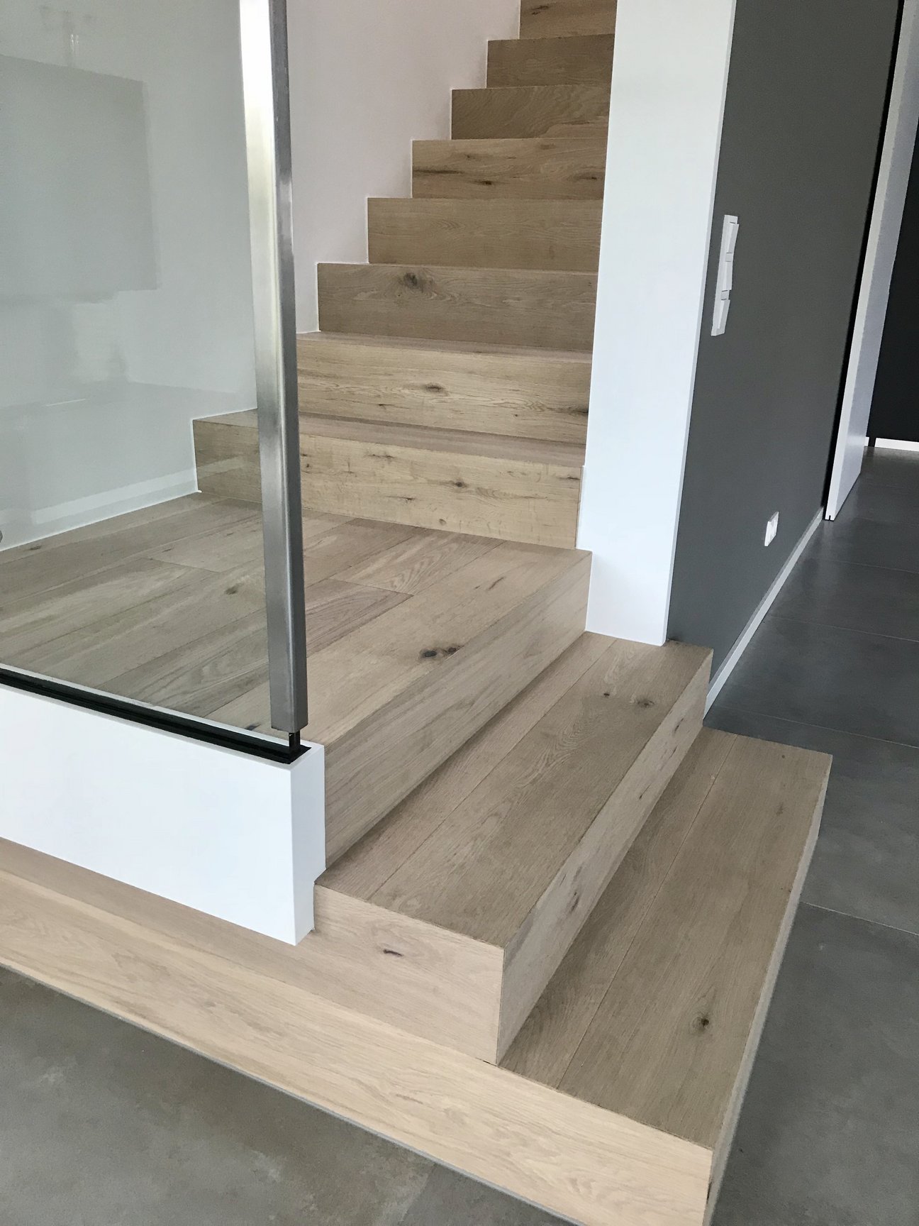Mit weiß geölter rustikaler Eiche verkleidete Treppe mit Glasgeländer